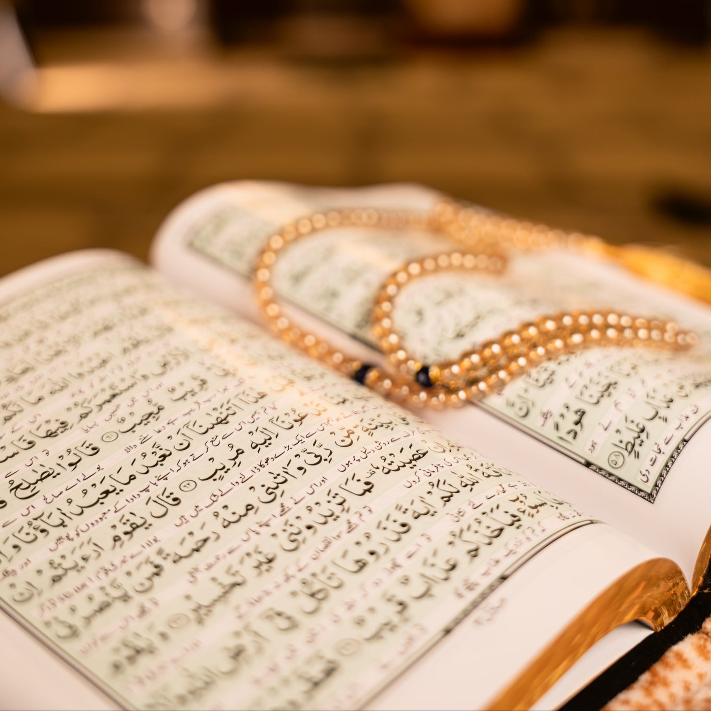 Open book with Arabic text and a rosary on a blurred background