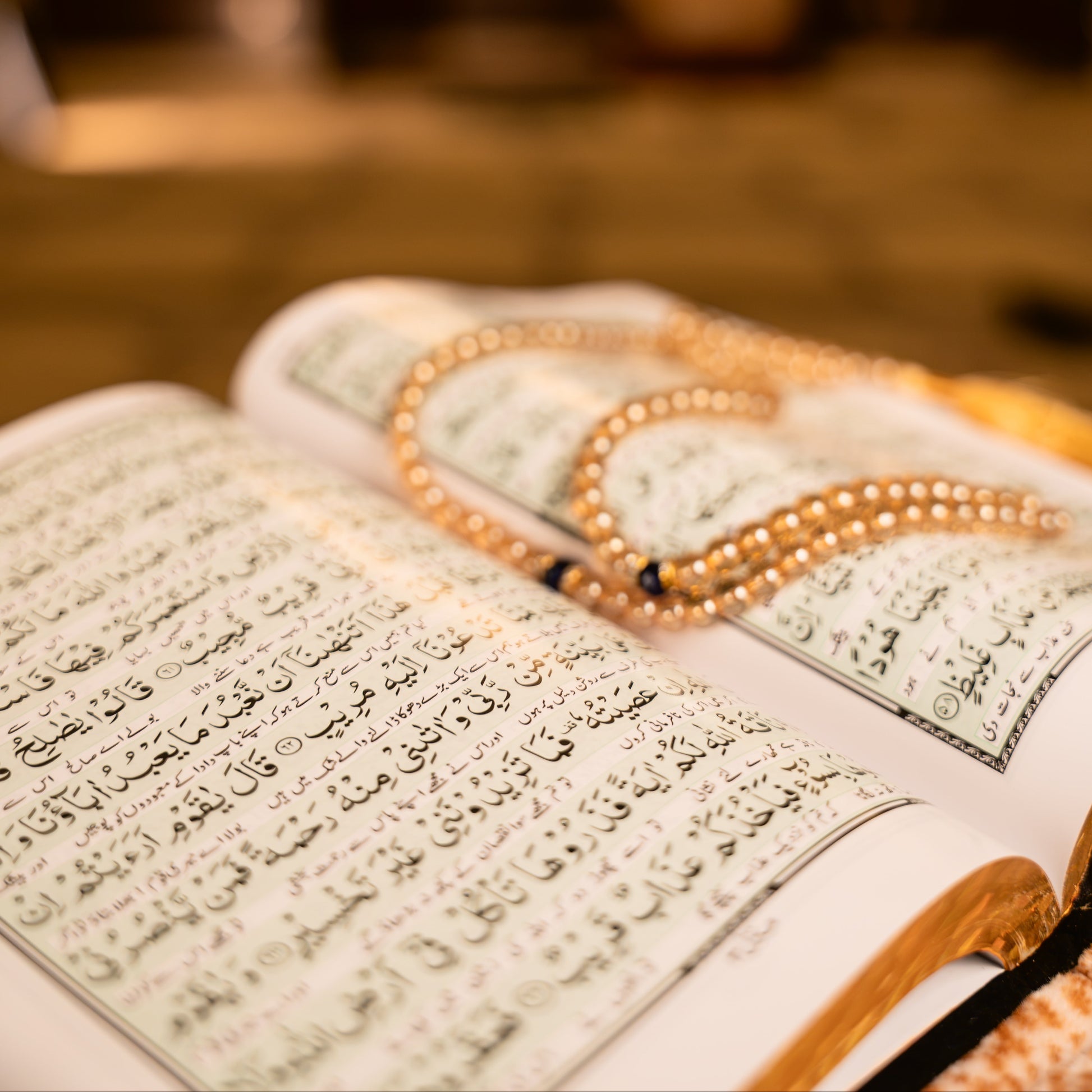 Open book with Arabic text and a rosary on a blurred background