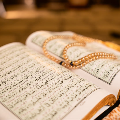 Open book with Arabic text and a rosary on a blurred background